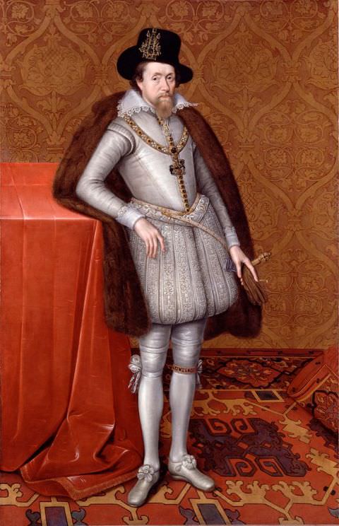 Painting. A colourful, full-length portrait of a man standing within an indulgent interior, which has orange, patterned walls and a red patterned rug. He is wearing silver, fitted clothing, a brown cape, and a black hat. 