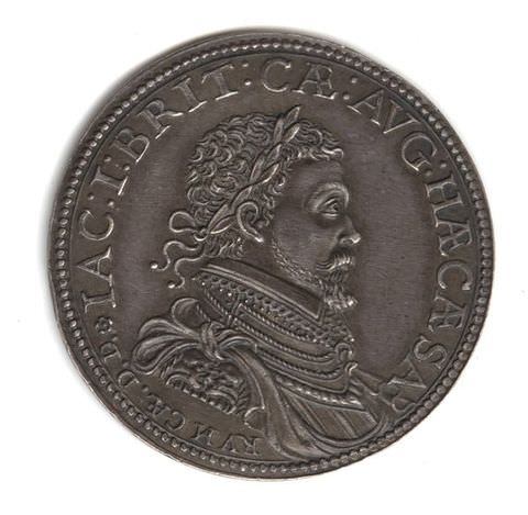 Colour photograph. A dark brown coin photographed on a white background. The coin features text encircling its circumference. In the centre is the profile portrait of a man with curly hair and a wreath tied around his head.