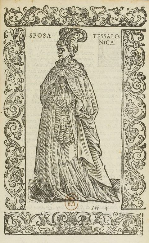 Page of a book. This black and white book illustration is surrounded by an ornately decorated frame featuring three-dimensional, organic shapes. Within the frame stands a woman wearing a long dress covered with a cape, and an ornate headdress. Text on the upper right of the image reads ‘ETHIOPO SOLDATO.’ 